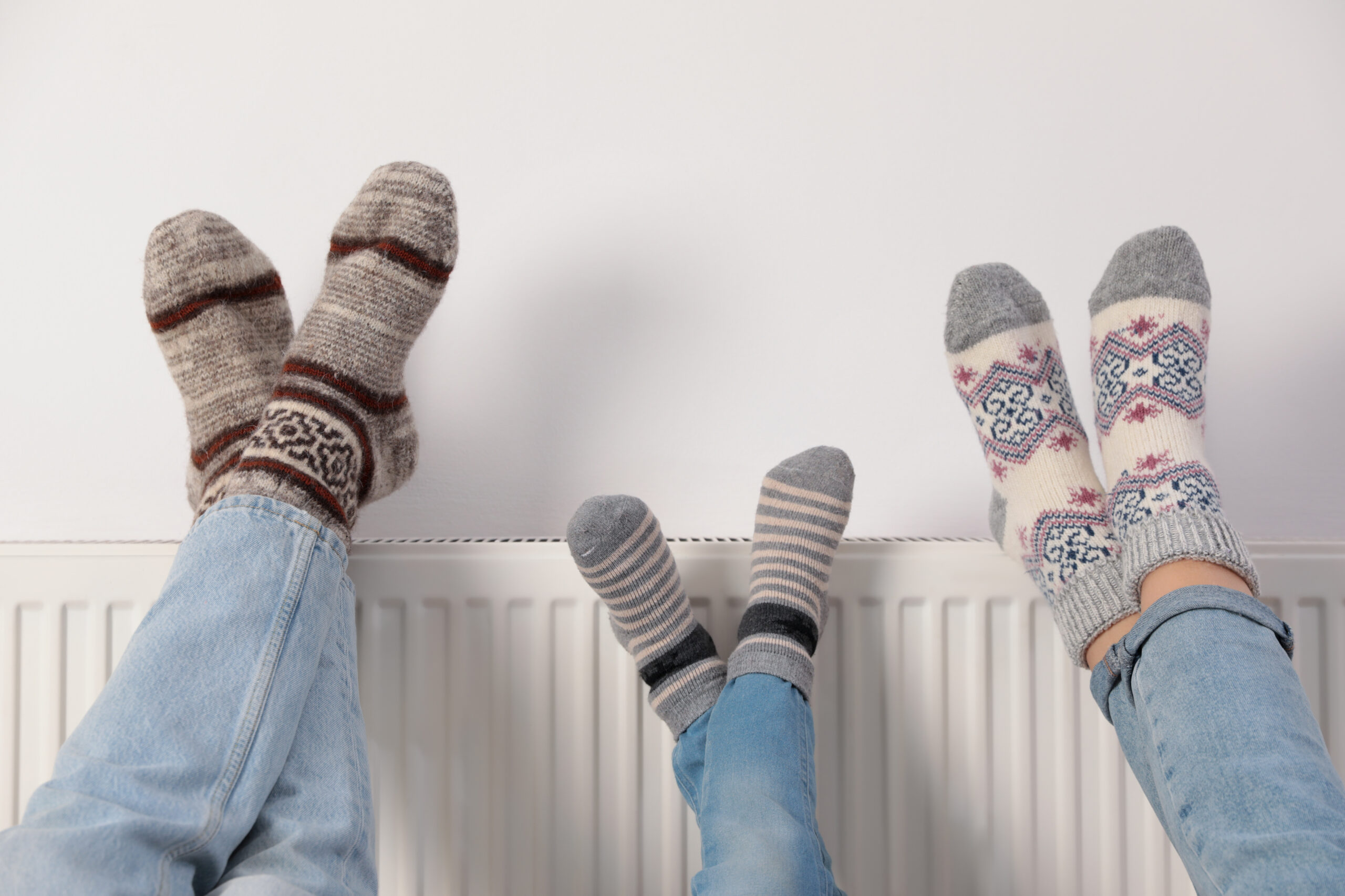 Family warming legs on heating radiator near white wall, closeup
