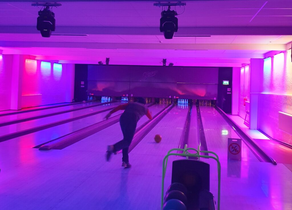 Spieler auf Bowling Bahn in rosa Licht mit Ball werfen